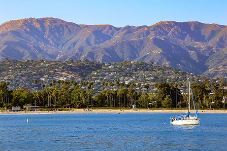 View of Santa Barbara Harbor from the water with a single sailboat and mountains in the background.